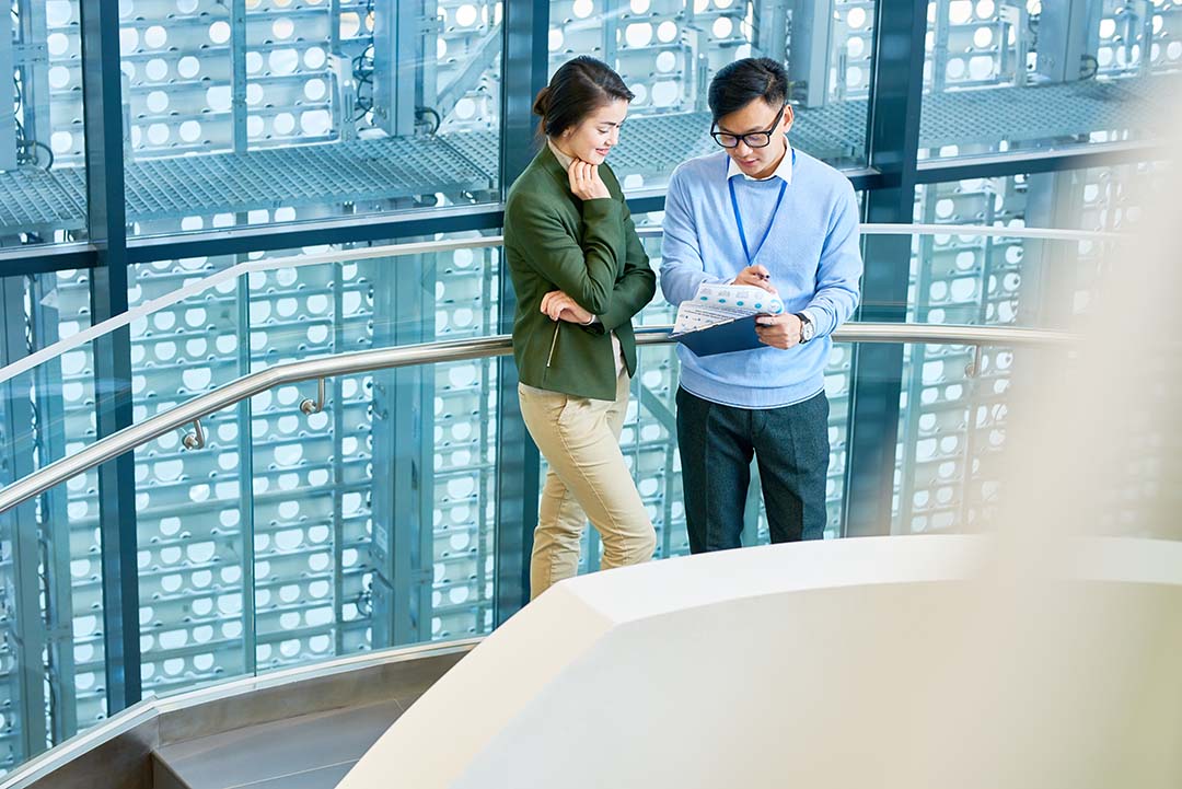 Portrait of two Asian business people, man and woman, standing at staircase in modern office building, copy space